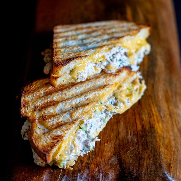 Grilled tuna melt sandwich with melted cheese and grill marks, cut in half on a wooden board.