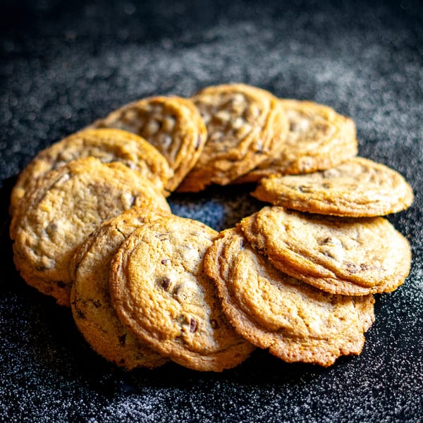 A circular arrangement of golden-brown chocolate chip cookies on a dark, sugar-dusted surface.