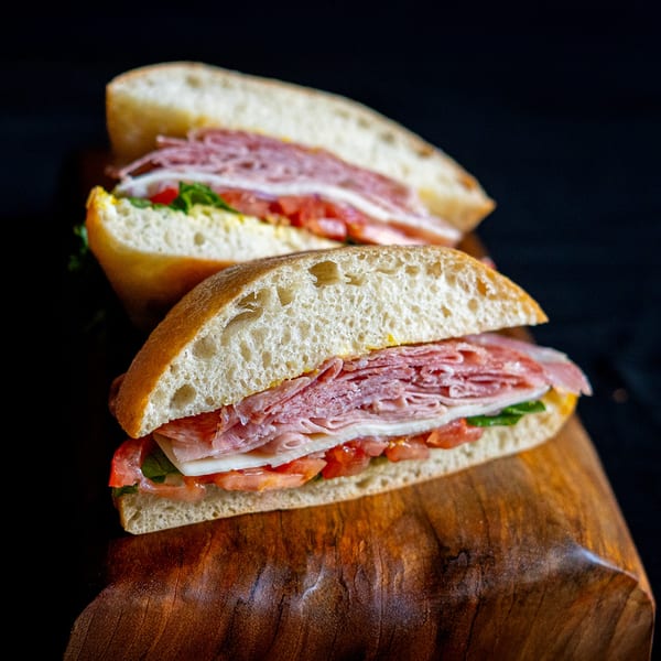Two Domenico's Delicatessen sandwiches with meat, cheese, tomatoes, and lettuce on a wooden board.