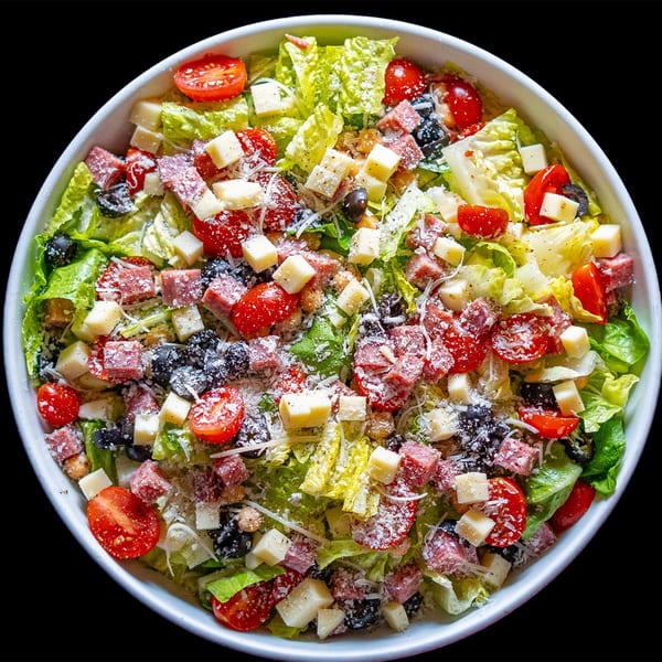 A vibrant Domenico's Delicatessen salad with lettuce, tomatoes, olives, cheese cubes, and deli meat.